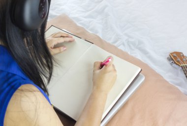 Women or girl sit on bed, listen to music and writing down on blank note book