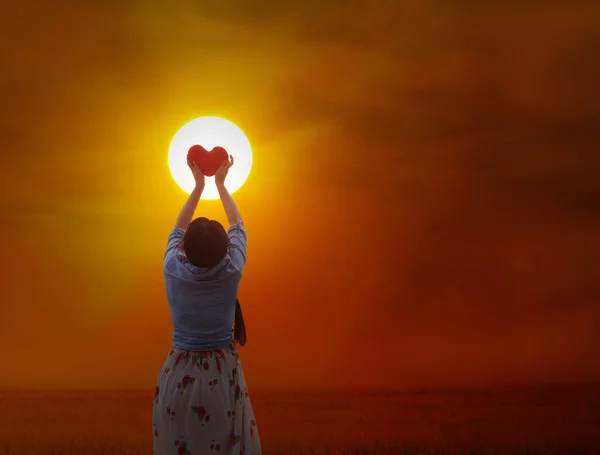 Las mujeres suavemente sostienen el corazón rojo al sol — Foto de Stock