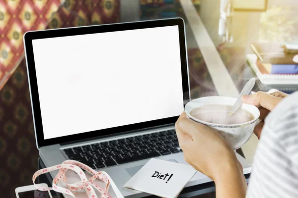 Tea in girl hand with blank screen laptop and measure tape