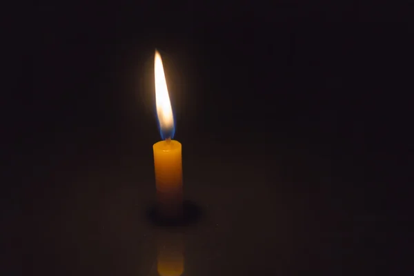 Одинокая простая свеча, зажженная на темном фоне — стоковое фото