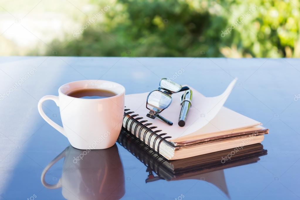 Classic white cup of black coffee decorated with note and pen with green nature background