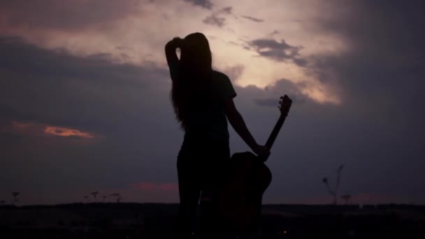 Silhueta de uma menina com uma guitarra ao pôr do sol — Vídeo de Stock