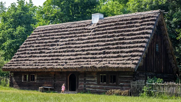OPOLE, POLAND - June 20, 2021:A little girl standing in front of a traditional, wooden house, on sunny summer day, in an open-air museum The Opole Village. 