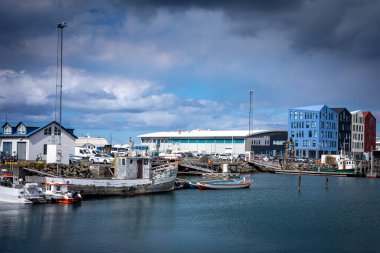 HAFNARFJORDUR, ICELAND - 16 Temmuz 2021: Hafnarfjordur balıkçı limanı - küçük tekneler ve renkli liman binaları. Gökyüzünde fırtınalı bulutlar. 