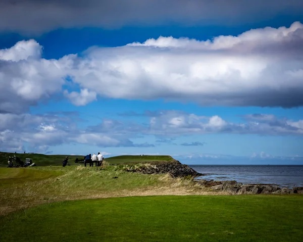 Golf oyuncuları, Hafnarfjordur, İzlanda 'daki yeşil golf sahasında deniz manzaralı bir bankta dinleniyorlar.
