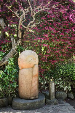 Beautiful Jizo stone statue under a flowering tree, at Hasedera buddhist temple garden, Kamakura, Japan.