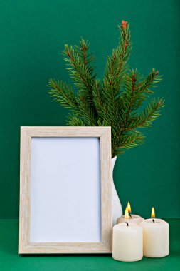 Mockup. Christmas. Decorative arrangement featuring an empty wooden frame, lit candles, and fresh evergreen branches, creating cozy and inviting atmosphere perfect for seasonal decor. Vertically