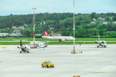 Ivan Paul II Havalimanı, Krakow, Polonya - 07 Mayıs 2025: Sarı taksici aracıyla havaalanı pistine park etmiş uçaklar, yoğun havacılık ortamı ve arka planda yemyeşil manzaralar sergiliyor