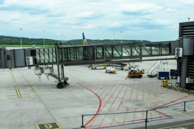 Ivan Paul Havaalanı, Krakow, Polonya - 07 Mayıs 2025: Asfalt üzerindeki uçağa bağlı jet köprüsü, modern mimari ve yoğun seyahat ortamını gösteren havaalanı görüntüsü