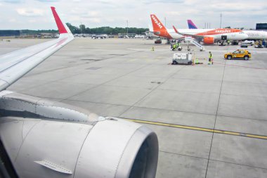 İvan Paul II Havalimanı, Krakow, Polonya - 07 Mayıs 2025: Birden fazla uçak, yer ekibi ve görev araçlarıyla dolu yoğun havaalanı pistine bakan uçak kanadı manzarası