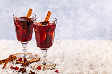 Sıcak şarap. Zarif bardaklarda sunulan bayram içecekleri, tarçın çubukları ve yıldız anasonlarıyla süslenmiş, karlı yüzeye yerleştirilmiş, kış kutlamaları için sıcak ve davetkar atmosfer yaratıyor.