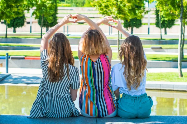 Moms and daughters sit with their backs to the camera and show with their hands a heart symbol. girls and women love each other. family, mother\'s day, female friendship