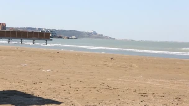 Paar ligstoelen en een parasol op een verlaten strand perfecte vakantie concept. Verlaten kust plaats met oude boot wrak, vissershuis, dienst rails schot in zonnige dag met een blauwe hemel. — Stockvideo