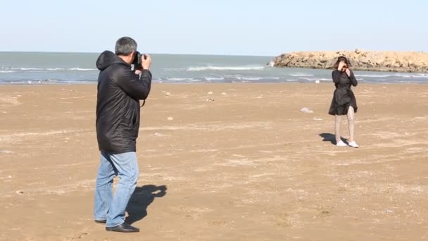 Hombre tomando fotos de una hermosa mujer en la playa . — Vídeos de Stock