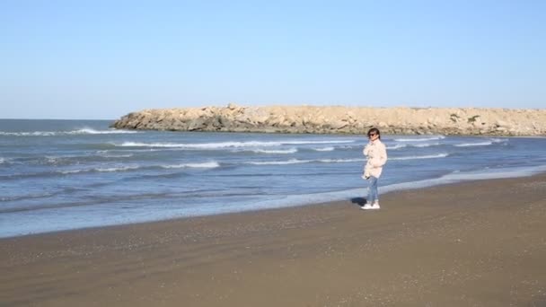 Depressed young woman near the sea in a windy day. Beautiful young brunette woman outdoors portrait near the sea. Young pretty girl in pink dress walking near the seaside at sunset. sandstorm — Stockvideo