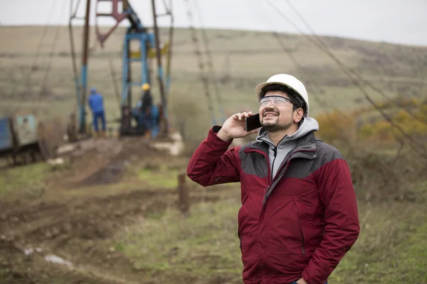 Trabajador petrolero en uniforme y casco, con teléfono móvil . — Foto de Stock