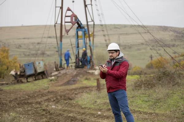 Trabajador petrolero en uniforme y casco, con teléfono móvil . — Foto de Stock