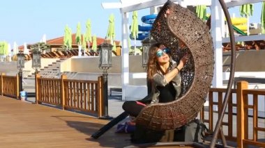 Bir hasır salıncak aqua park üzerinde oturan bir bayan. Kadın parkta güneşli yaz günü askıya bir hasır sandalye sürme gözlük.