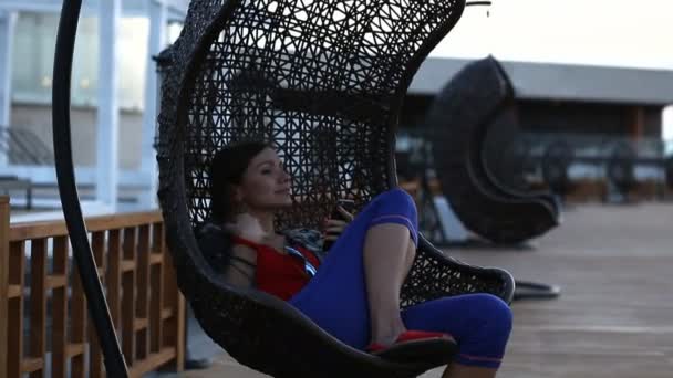 Woman sitting on a wicker swing aqua park. Woman in glasses riding in a wicker chair suspended in the park sunny summer day.