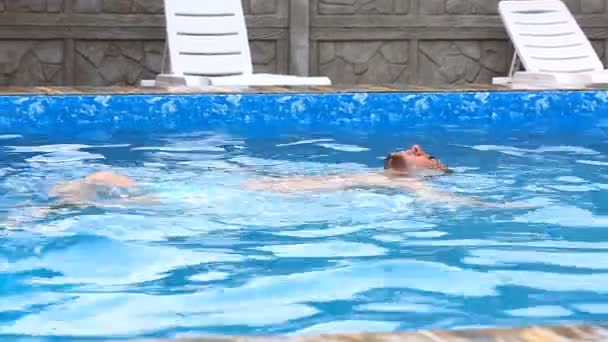 スイミング プールで水の上に浮かんでいる男。晴れた日には、スイミング プールでリラックスした若い男. — ストック動画