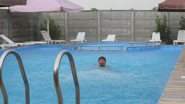 Hombre flotando en el agua en la piscina.Joven relajándose en la piscina un día lluvioso — Vídeo de stock