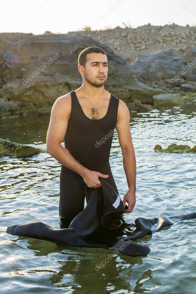 A young surfer putting on his wetsuit on the beach. Man in a suit