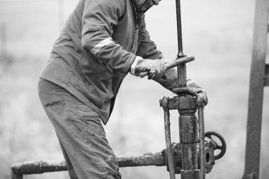 Oil workers check oil pump. Roustabouts doing dirty and dangerous work on an oil well servicing rig. clipart