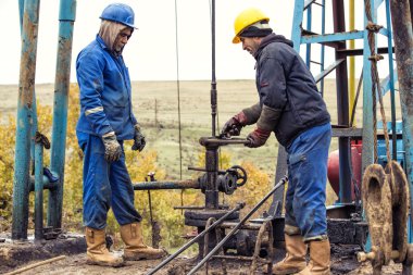 Petrol İşçileri petrol pompa kontrol edin. Roustabouts bir petrol kuyusu sondaj platformu hizmet işi pis ve tehlikeli. Kasım 2015 Şabran, Azerbaycan