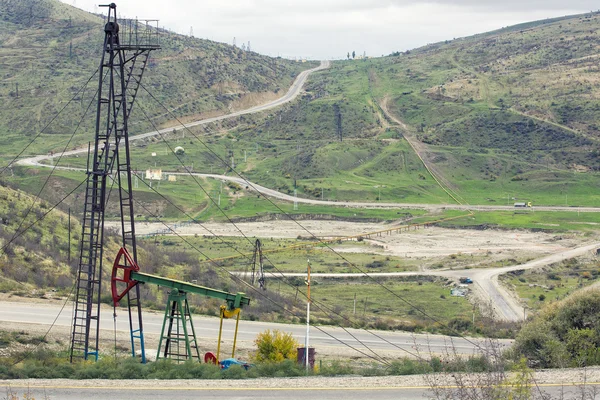 Oil pumps at large oilfield over mountain range. An oil well servicing rig sets up in mountainous country. A cluster of pumping units (oil wells) located in the foothills of the Shabran, Azerbaijan. — Stock Photo, Image