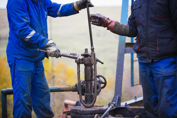 Oil workers check oil pump. Roustabouts doing dirty and dangerous work on an oil well servicing rig. — Stock Photo, Image