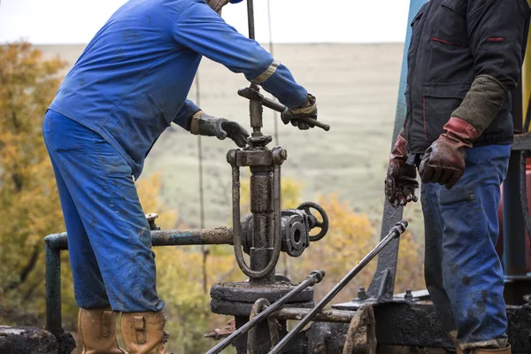 Trabajadores petroleros revisan bomba de aceite. Roustabouts haciendo trabajo sucio y peligroso en una plataforma de mantenimiento de pozos de petróleo . — Foto de Stock