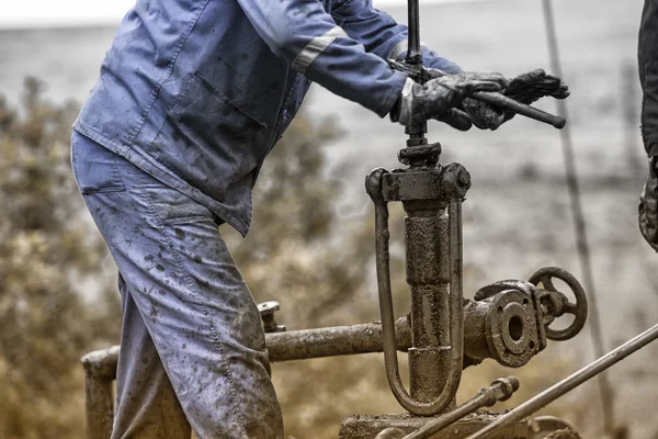 Os trabalhadores do petróleo verificam a bomba de óleo. Roustabouts fazendo trabalho sujo e perigoso em um equipamento de manutenção de poços de petróleo . — Fotografia de Stock