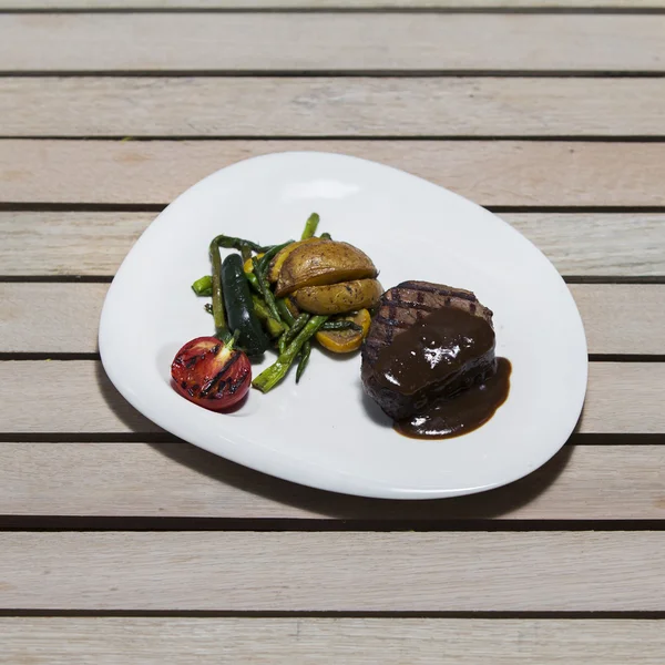 Köstliches Rindersteak auf Holztisch, aus nächster Nähe. Kalbssteaks vom Grill mit Gemüse auf Schneidebrett. — Stockfoto