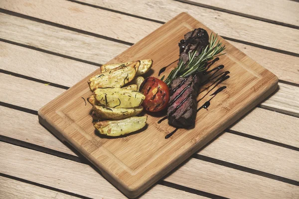 나무 테이블에 맛 있는 쇠고기 스테이크 클로즈업. 커팅 보드에 야채와 구운된 송아지 고기 스테이크. — 스톡 사진