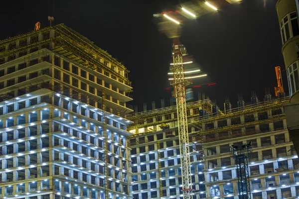 Muitos guindastes de torre constroem grandes edifícios residenciais à noite. edifícios em construção com guindastes e iluminação à noite escura. fotografia noturna de equipamento de construção no estaleiro . — Fotografia de Stock