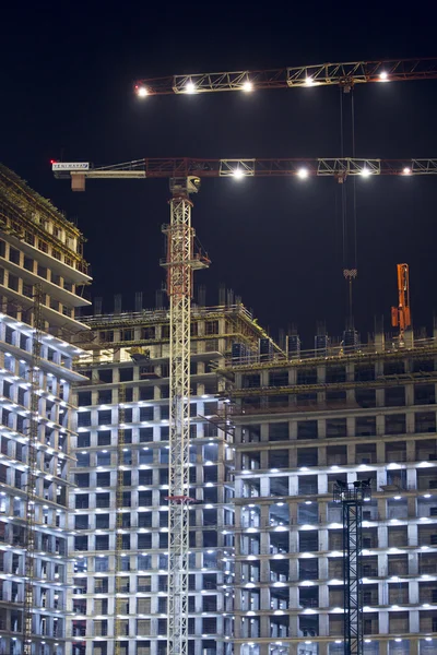 Muchas grúas torre construyen grandes edificios residenciales por la noche. edificios en construcción con grúas e iluminación en la noche oscura. disparo nocturno de equipo de construcción en el sitio de construcción . — Foto de Stock