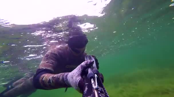 L'uomo nuota e pesca con la lancia nel mare Mediterraneo. Pescatore subacqueo che manovra il fucile mentre si tuffa verso la superficie. Passando attraverso le alghe Hardcore e vedere erba. Con suono . — Video Stock