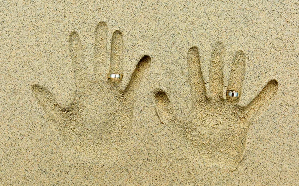 Two wedding rings placed on fingers in the sand — Zdjęcie stockowe