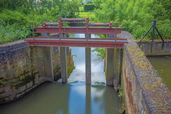 Impression of water flowing over a weir to control the water level of the Zwalmmolen, a water mill. Motion blur in the vegetation due to the long exposure.