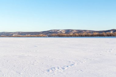 Geniş donmuş bir nehrin yüzeyi ve uzaktaki karşı kıyının..