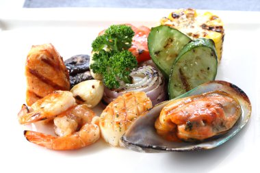 Beyaz çanak üzerinde kavrulmuş sebze ile ızgara deniz ürünleri