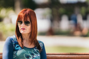 Bankta oturan kızıl saçlı kadın.