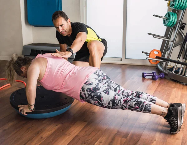 Entrenador personal ayudando a una mujer a hacer flexiones en interiores — Foto de Stock