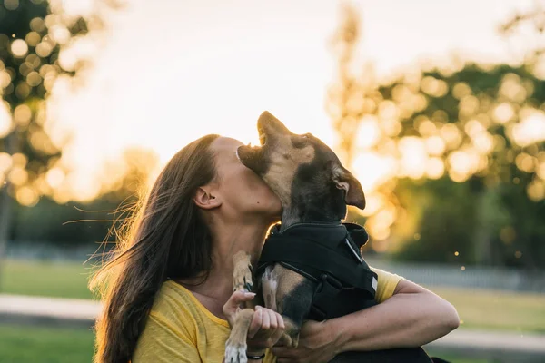 Parkta köpeğini öpen genç bir kadın.