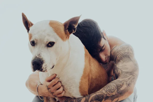 Dövmeli genç bir adamın portresi bir köpeği kucaklıyor.