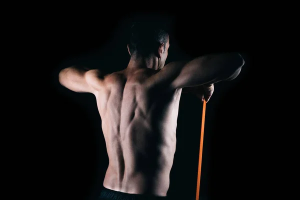 Costas de um homem forte exercitando com uma faixa elástica — Fotografia de Stock