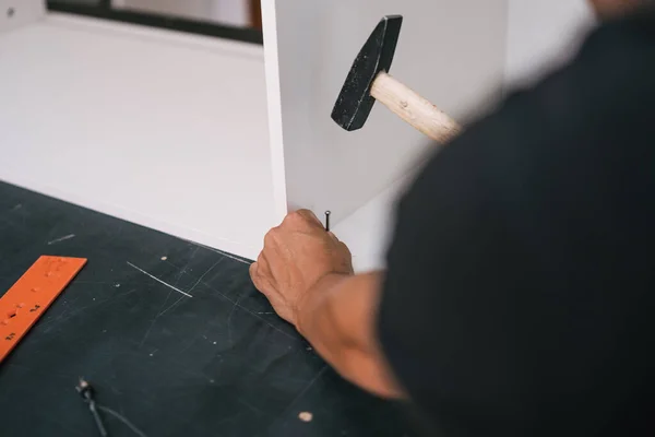 Mani inchiodare una vite con un martello in un pezzo di legno bianco di mobili — Foto Stock
