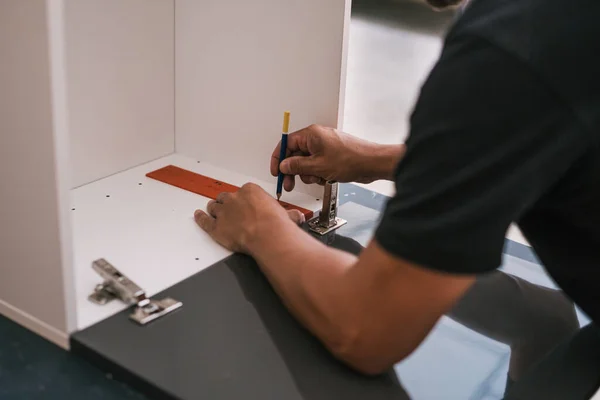 Mani di un uomo che segna una linea su un pezzo di legno di una cucina che sta assemblando — Foto Stock