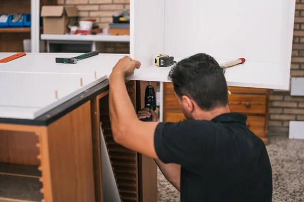 Worker using a drill to build a kitchen furniture — Stock Photo, Image