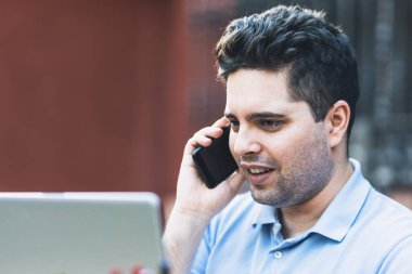 Adam bilgisayarla ticaret yaparken cep telefonuyla konuşurken gülümsüyor.